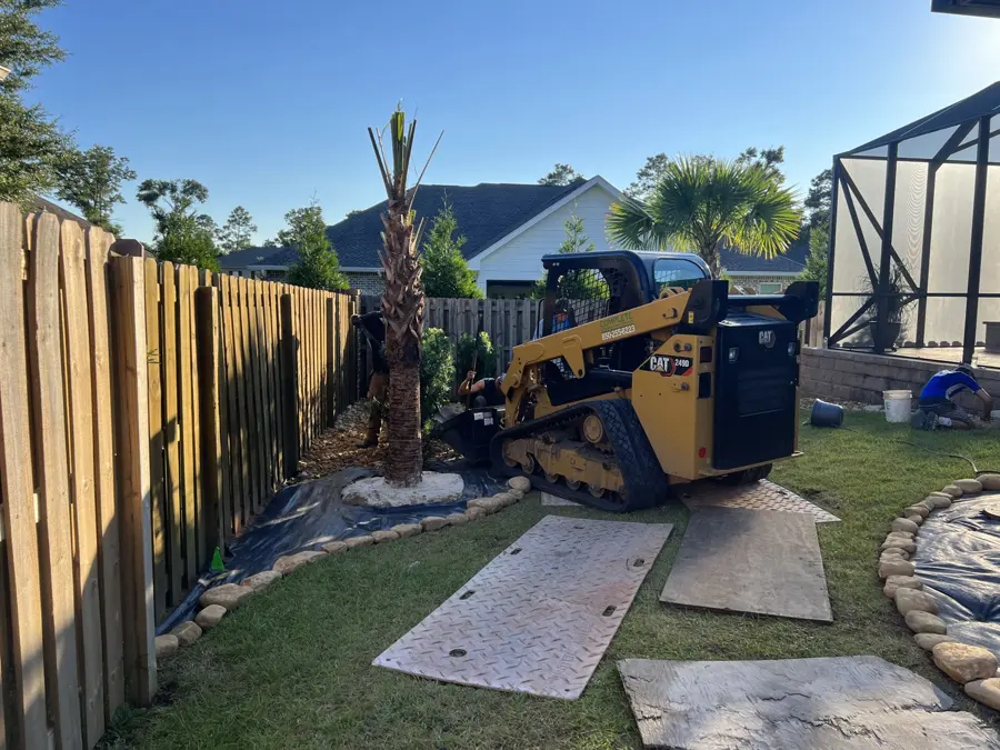Compact track loader finishing a landscape bed beside a fence